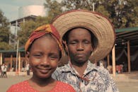 两个穿着传统服装和帽子的孩子在户外微笑，展示着文化多样性