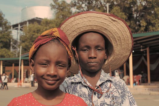 两个穿着传统服装和帽子的孩子在户外微笑，展示着文化多样性