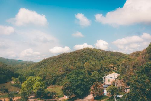 Free Scenic view of a rural Chinese landscape with a house, hills, and lush greenery under a bright blue sky. Stock Photo