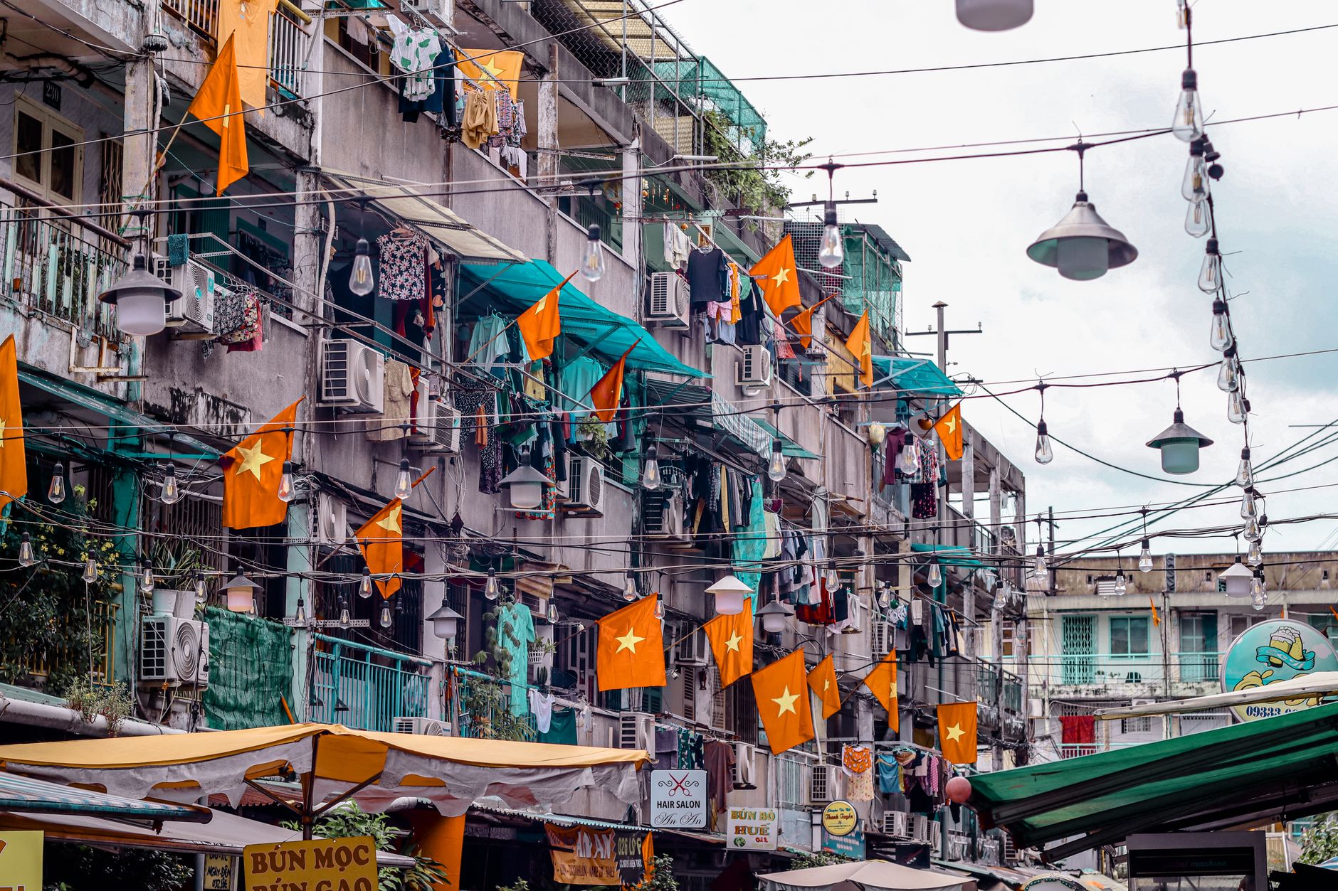 Vietnamese urban street scene with flags, laundry hanging, and outdoor market. A vibrant, everyday life depiction.