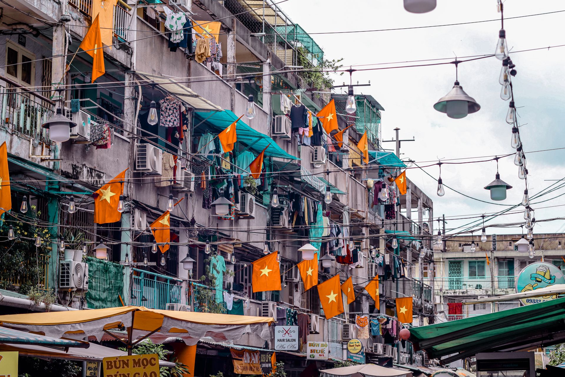 Vietnamese urban street scene with flags, laundry hanging, and outdoor market. A vibrant, everyday life depiction.
