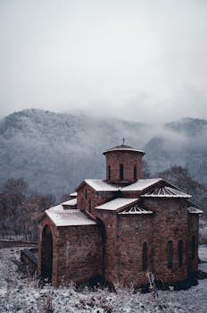 这座历史悠久的教堂被雪山和雾气环绕，呈现出宁静的冬日景象