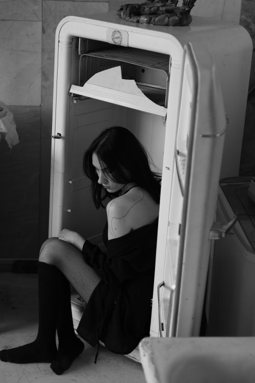 Free Moody black and white portrait of woman seated in open refrigerator, creating an artistic statement. Stock Photo