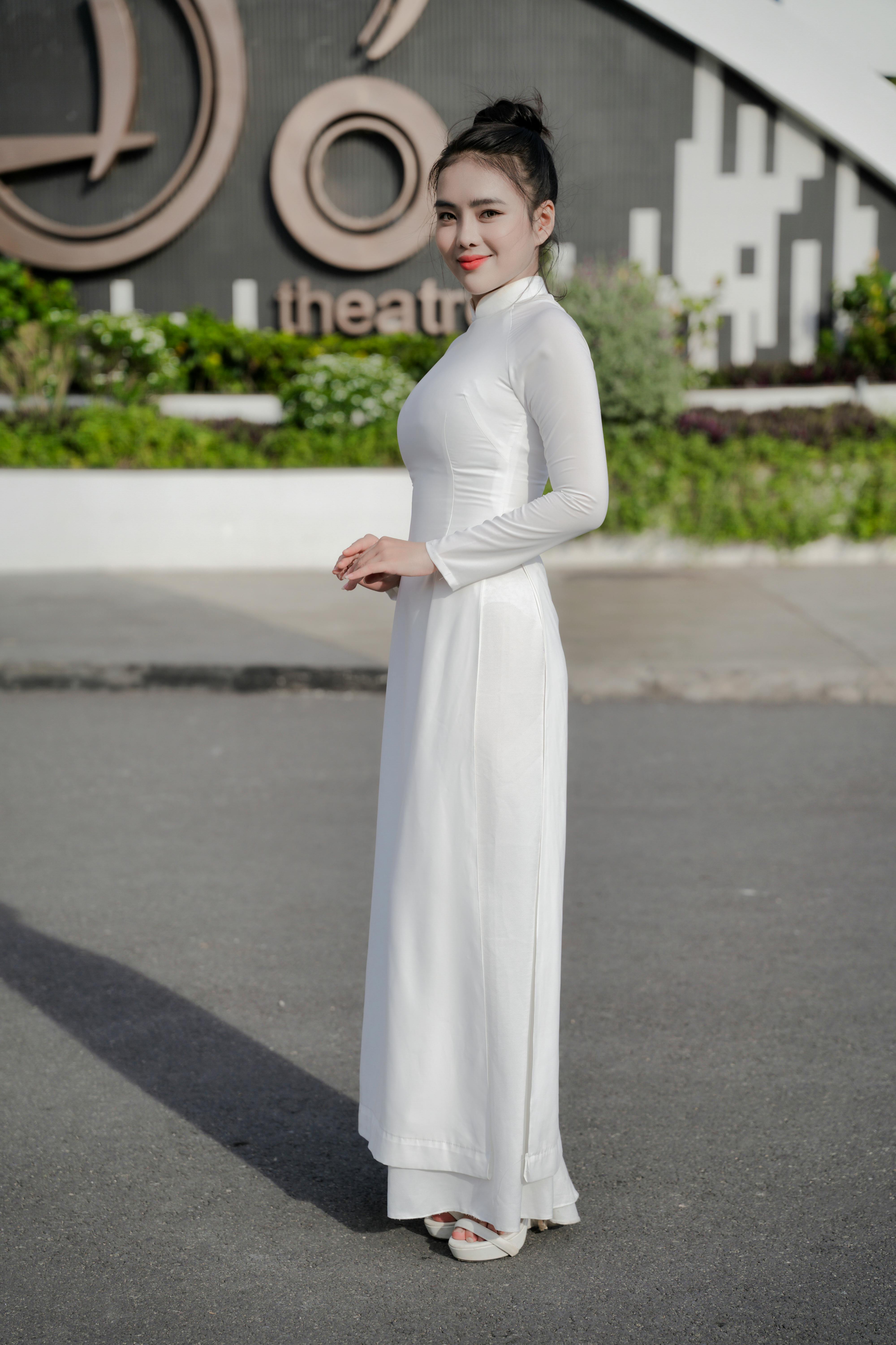 Ücretsiz Tiyatronun yakınında dışarıda duran beyaz ao dai elbiseli bir kadının yan görünümü. Stok Fotoğraflar