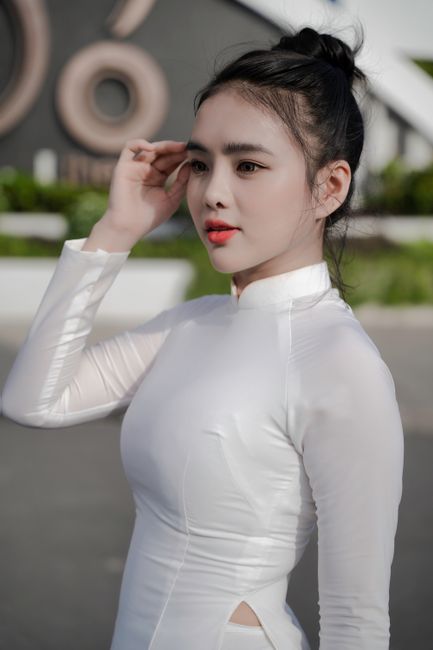 Portrait of a woman in a white Ao Dai dress, gracefully posing outdoors.