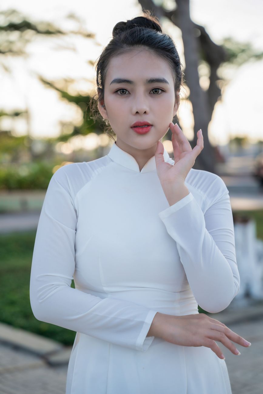 Portrait of a young woman in a white Áo Dài standing outdoors with a serene expression.