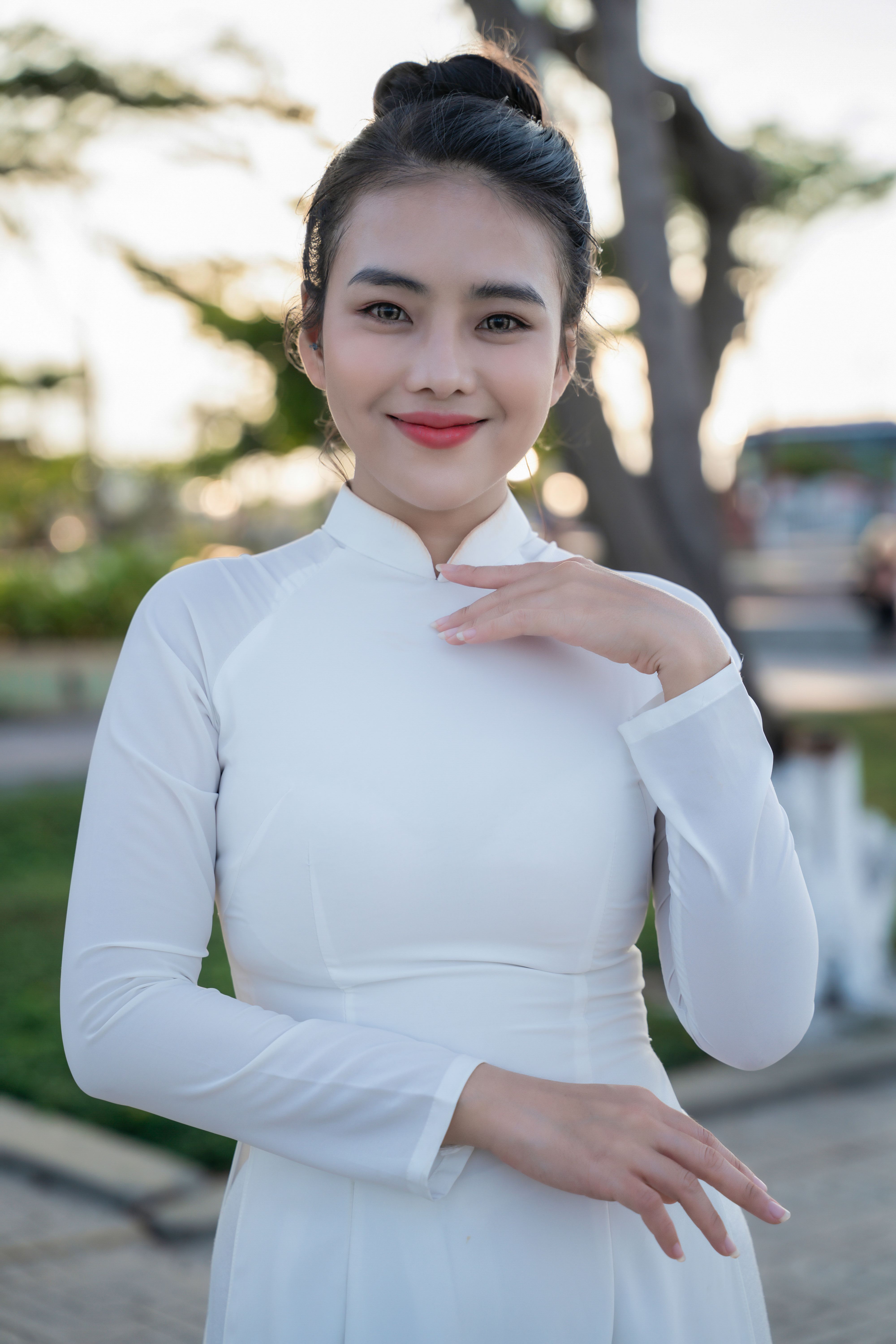 Portrait of a smiling woman in a white traditional dress with a blurred outdoor background.