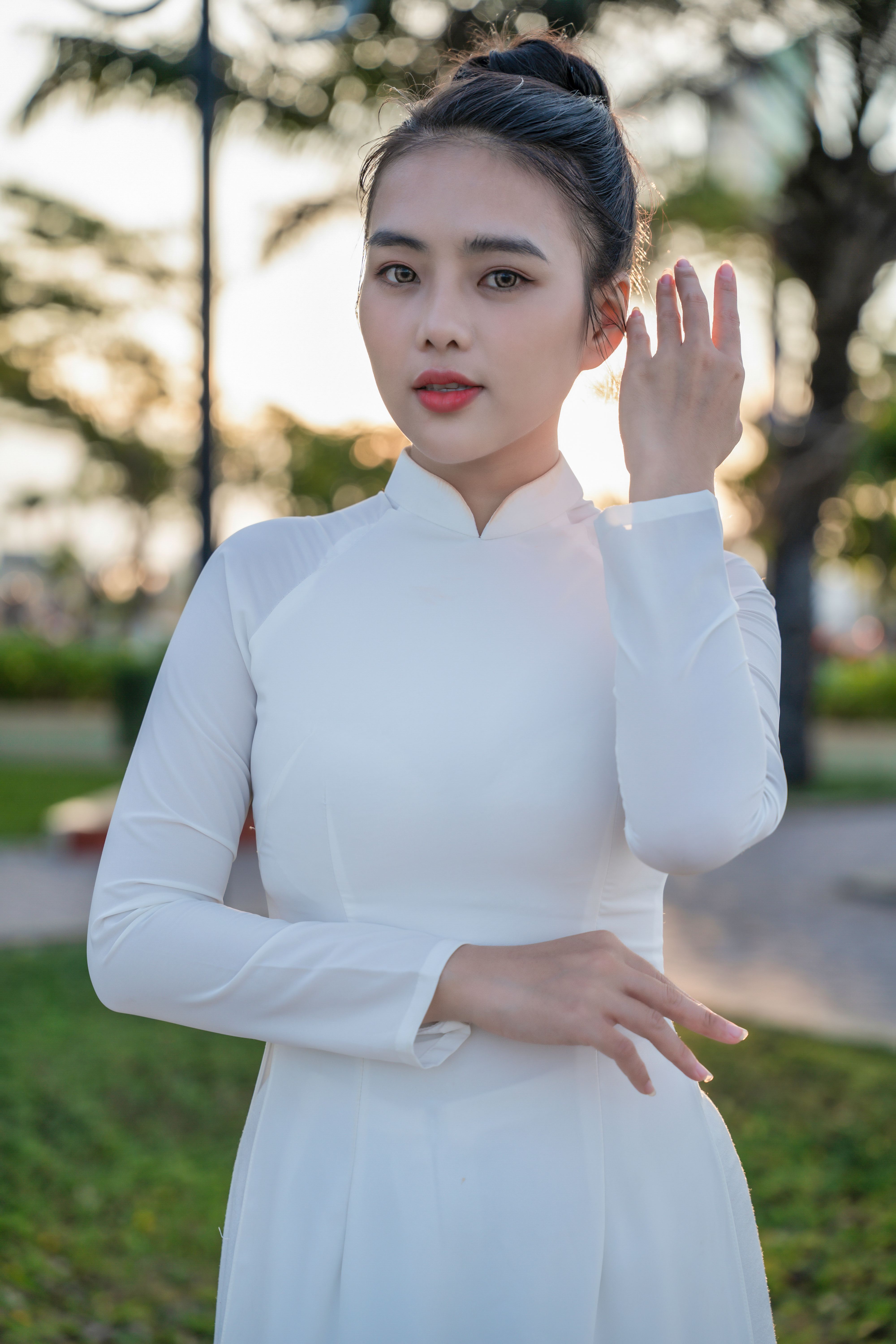 Woman in traditional white Ao Dai, posing gracefully outdoors with lush greenery.