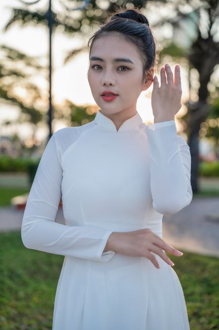 Woman in traditional white Ao Dai, posing gracefully outdoors with lush greenery.