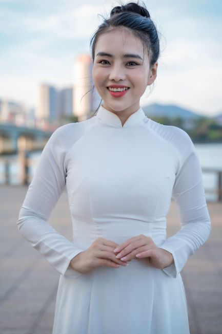 Elegant woman in an ao dai smiles brightly with an urban backdrop. Vibrant capture of culture.