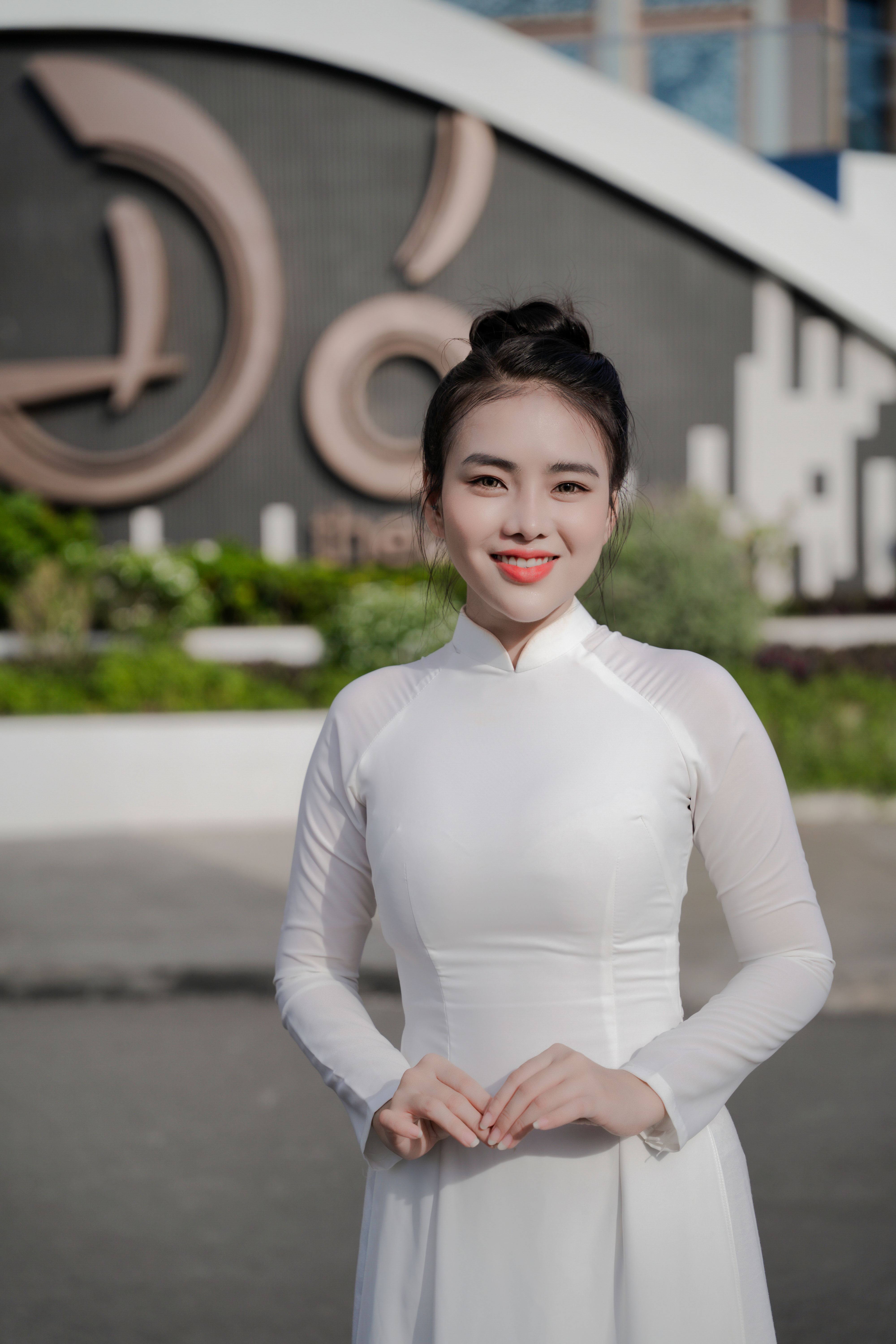 Woman in white Vietnamese ao dai smiling outdoors with a blurred background. Cultural representation.