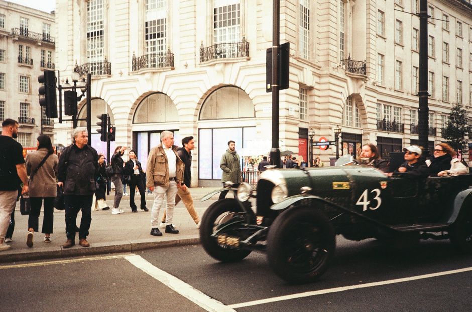 Vintage car driving past pedestrians in busy Piccadilly Circus, London, capturing urban life.