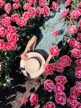A woman in a floral dress and sunhat relaxes amidst vibrant pink tulips in a garden.