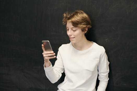 Smiling young woman with short hair using a smartphone indoors against a chalkboard.