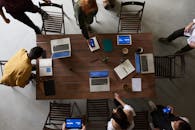 办公室环境中，团队围坐在桌旁，俯视视角下，大家正围绕着笔记本电脑集思广益