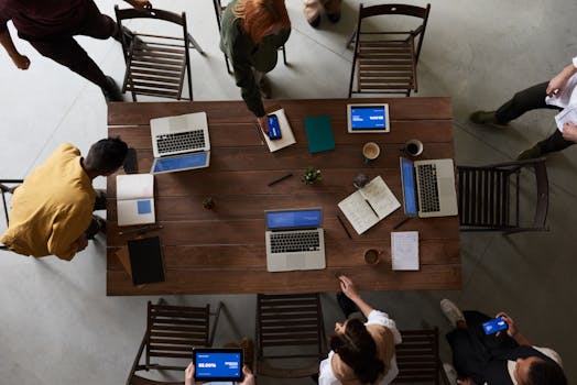 Overhead view of a team brainstorming around a table with laptops and notebooks in an office setting.