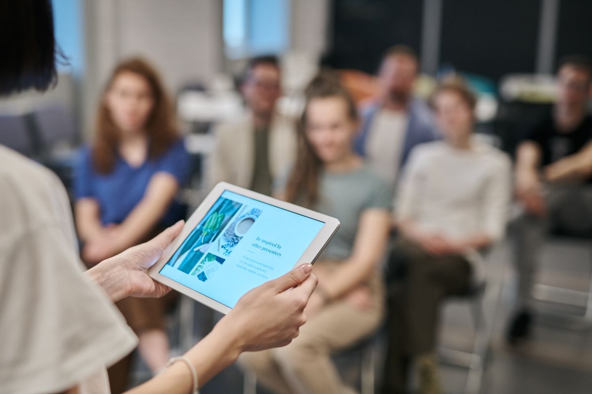 Formateur présentant sur tablette à un groupe d'apprenants adultes, illustrant les tendances de la pédagogie en formation professionnelle
