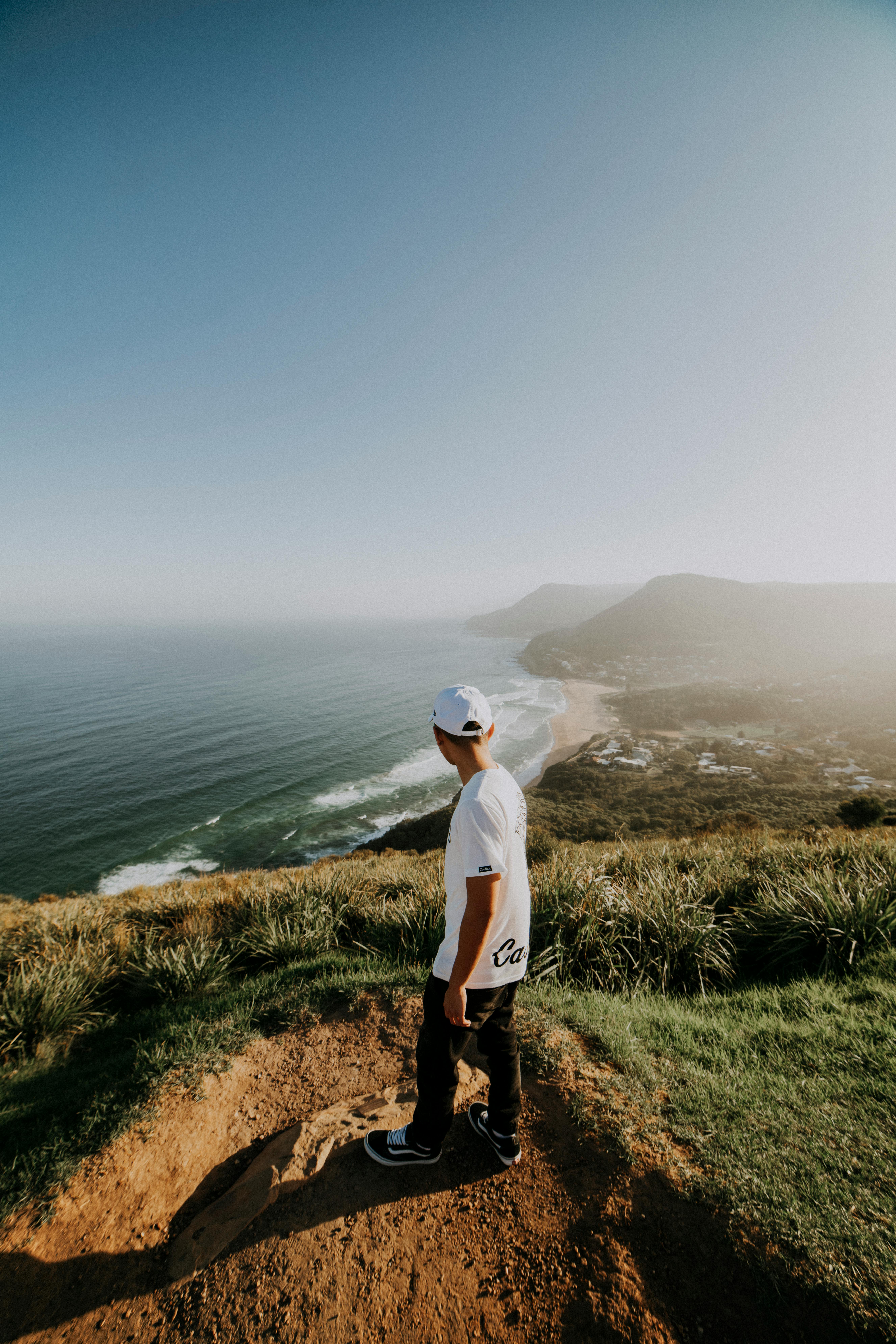 Young adult on a scenic clifftop with ocean view, clear skies, and vibrant greenery.