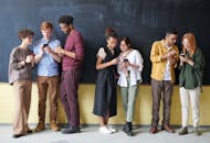 多元化的年轻人站在黑板前，用智能手机展示技术与连接