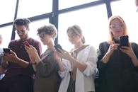 明亮的室内环境中，四名成年人微笑着与智能手机互动