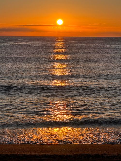 Free Stunning sunrise reflecting on a calm ocean with golden hues and a serene sandy beach. Stock Photo