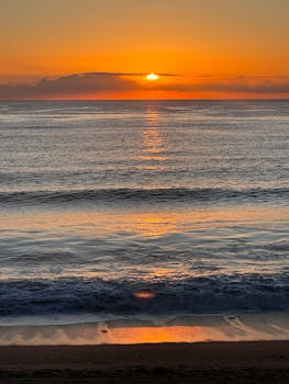 Captivating sunrise over tranquil ocean waves and sandy beach.