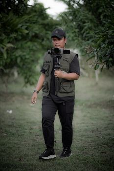 A cameraman holding a stabilizer, captured in a verdant outdoor environment.