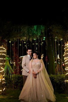 Captivating portrait of an Indian couple on their wedding day, elegantly posed under twinkling lights.