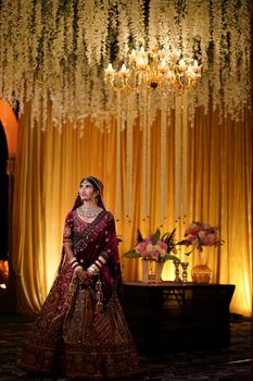 Beautiful Indian bride in stunning traditional attire, posing under a chandelier.