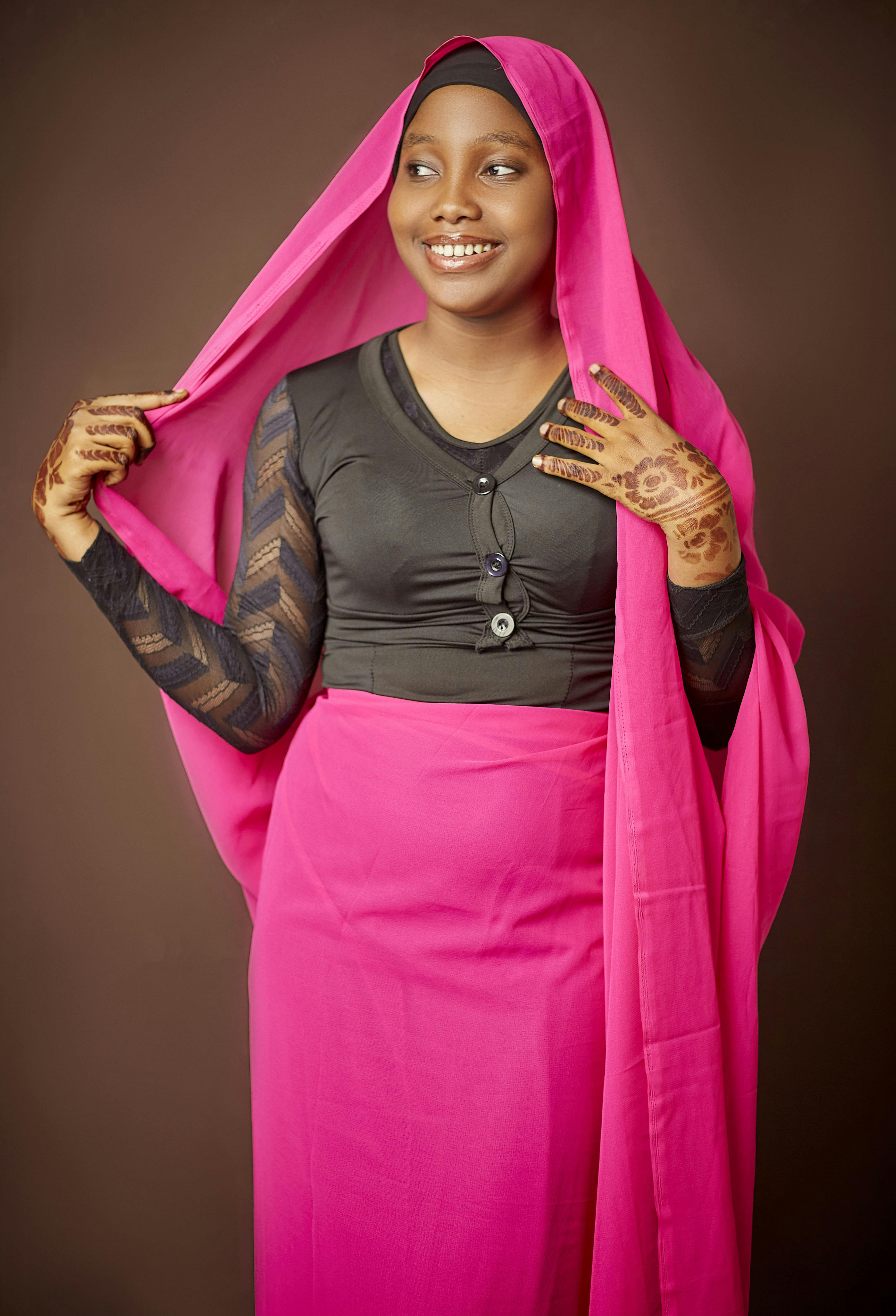 A woman smiles while wearing a pink hijab and henna designs on her hands.