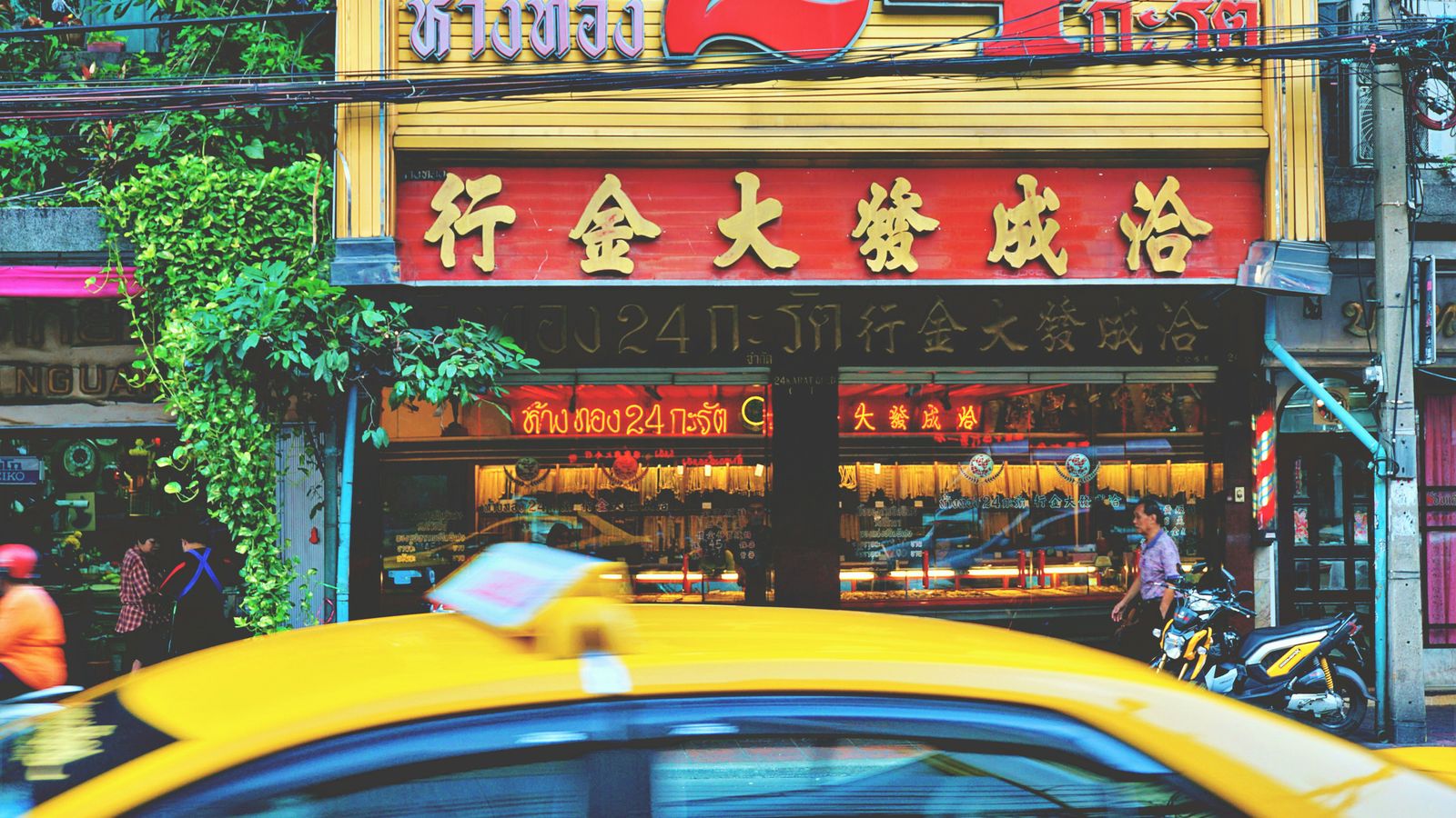 Colorful street scene in Bangkok's Chinatown featuring shops and a passing taxi.