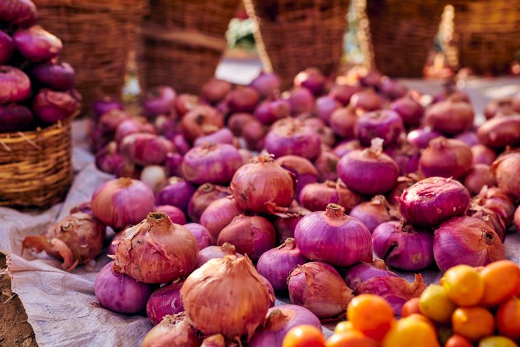 Red onions and tomatoes in wicker baskets at a market — photo by Kazys Photography on Pexels