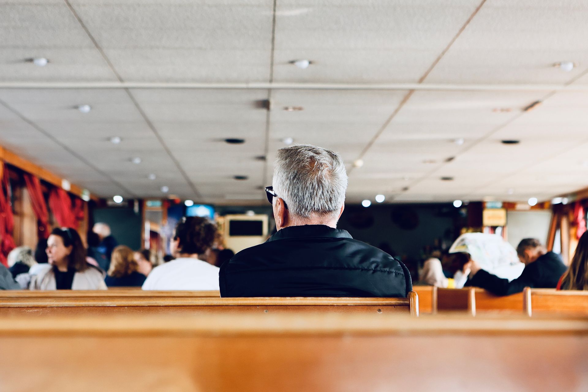 A senior man with gray hair sits inside surrounded by a diverse group of people.