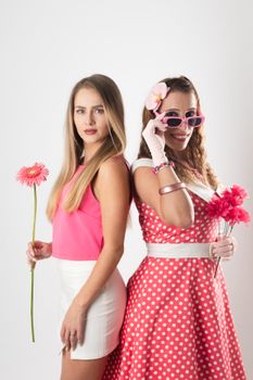 Two stylish women posing with pink fashion and flowers against a white backdrop.