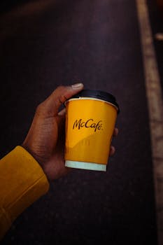 A person holding a yellow McCafé cup on a dark street, showcasing urban lifestyle.
