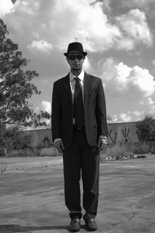 Free Black and white photo of a man wearing a suit and hat standing outdoors. Stock Photo