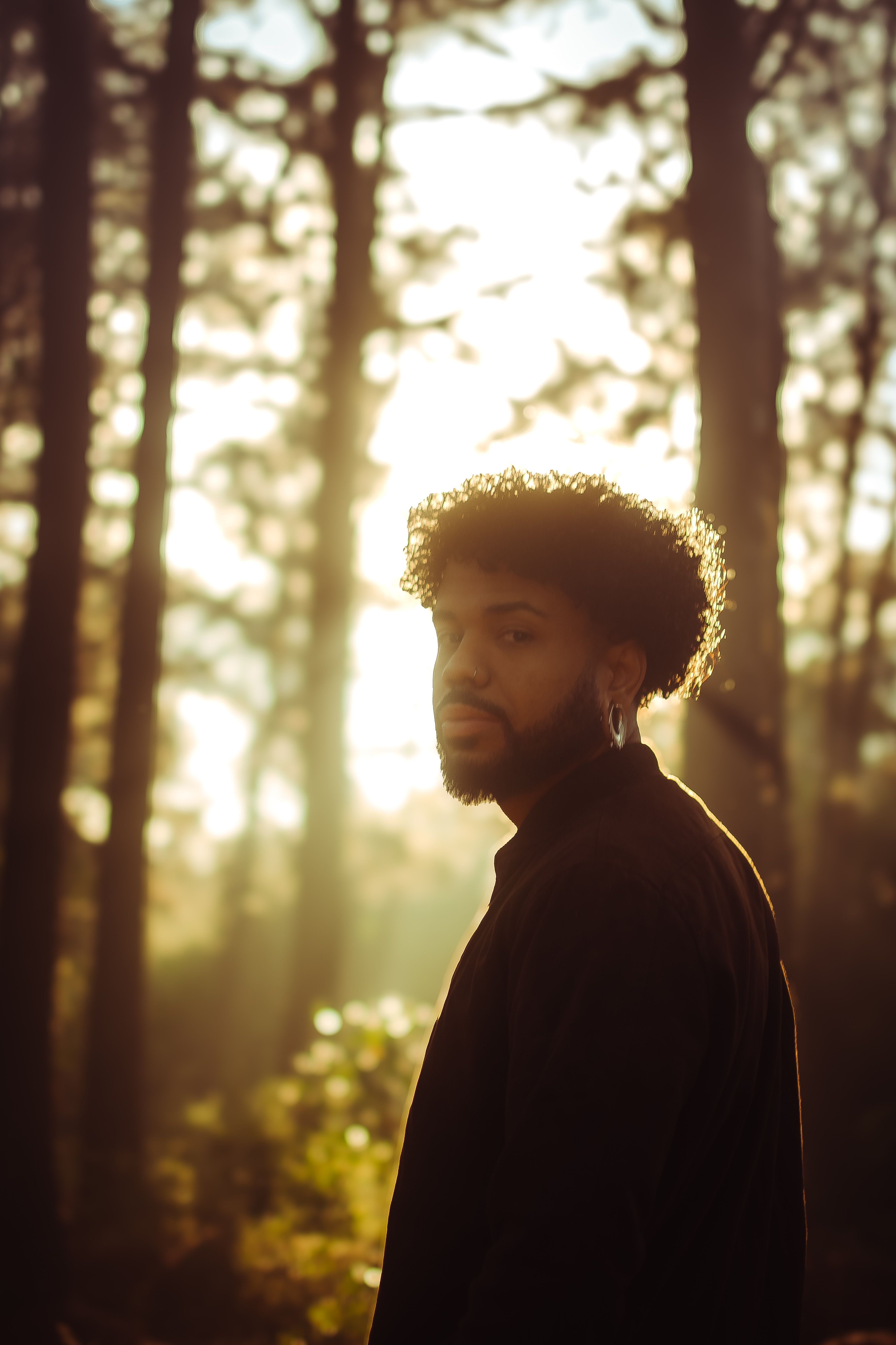 A contemplative man stands in a sunlit forest, capturing a moment of tranquility.