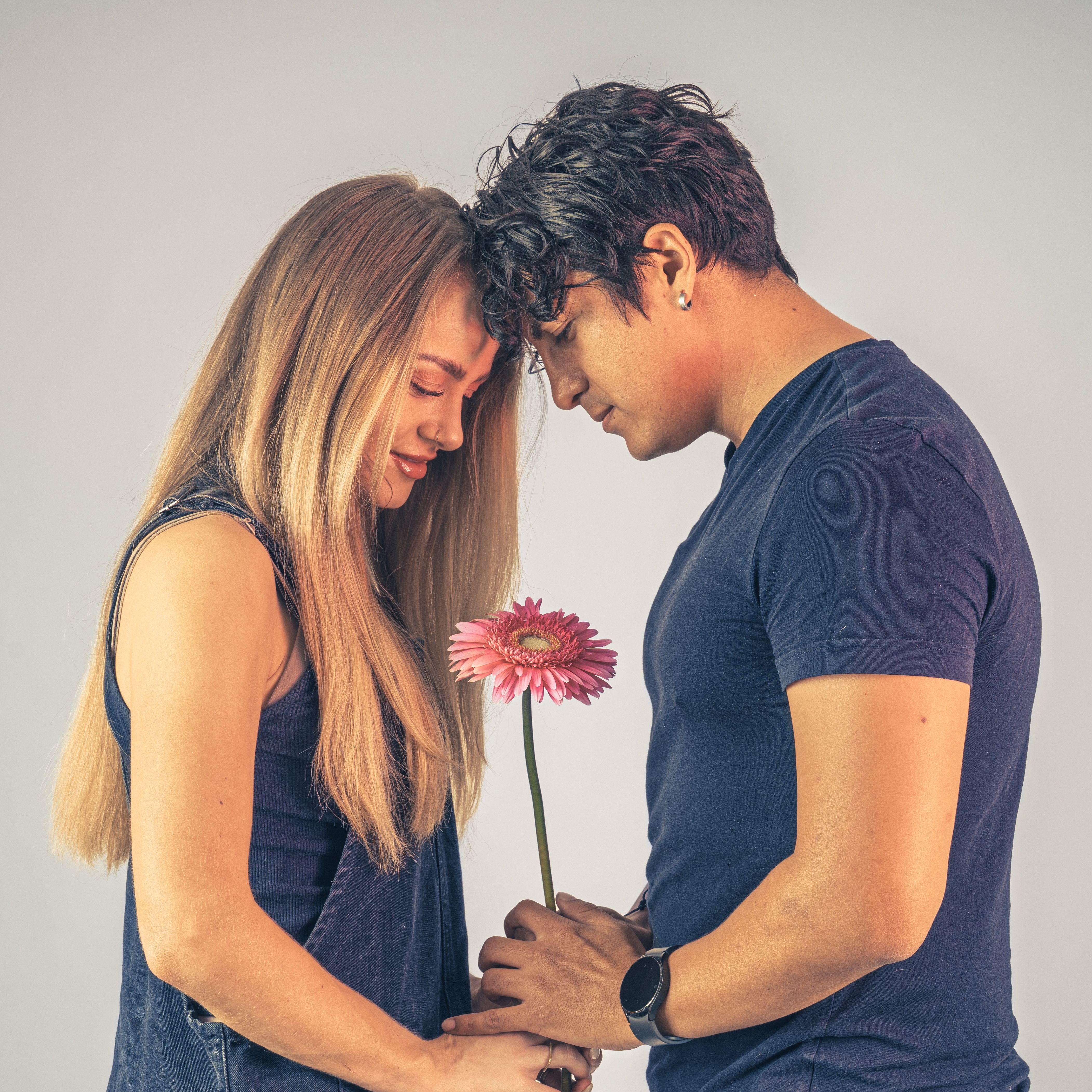 A tender moment between a couple sharing a pink gerbera daisy. Intimate and serene.