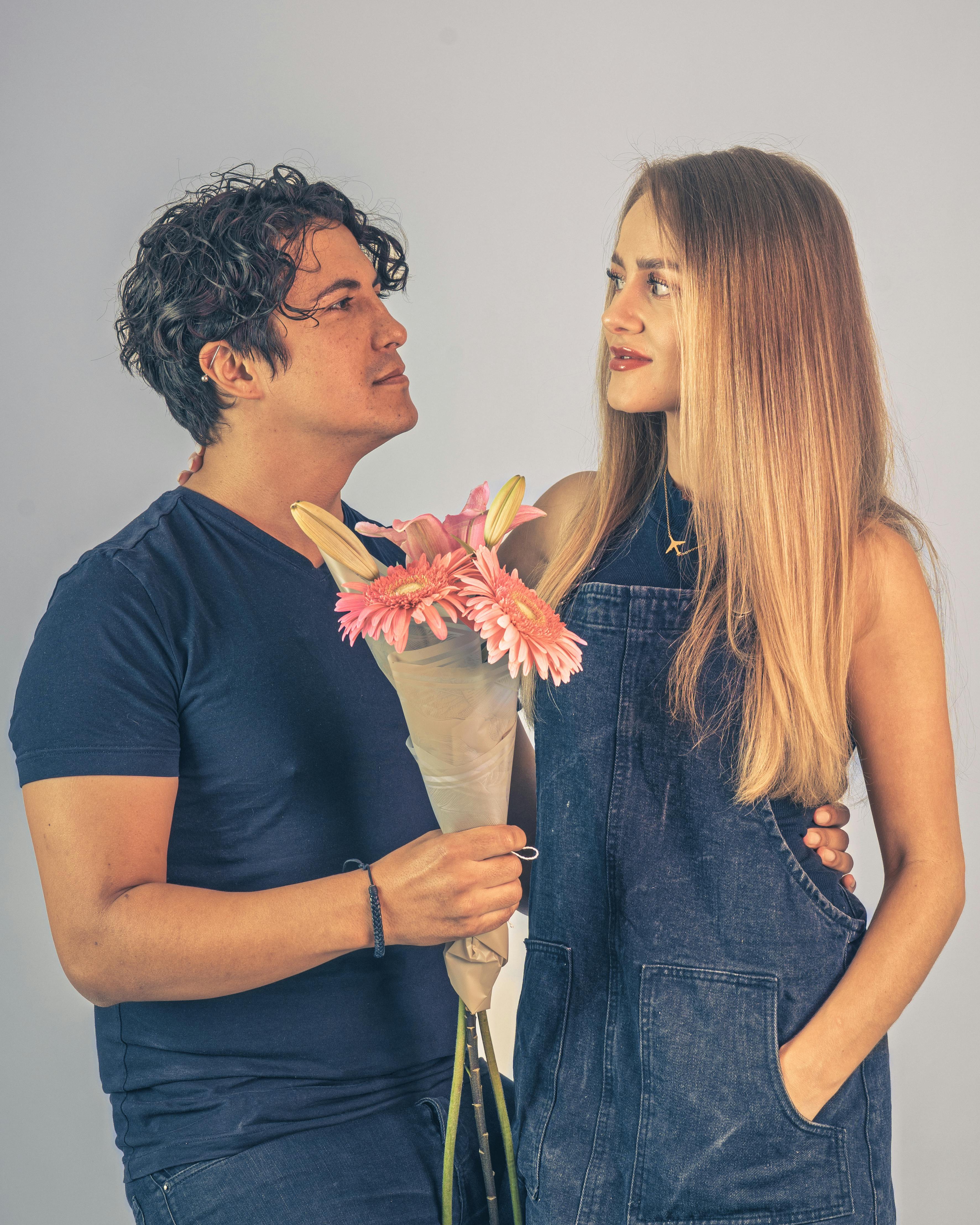 A young couple sharing a moment, embracing with a bouquet of pink flowers indoors.