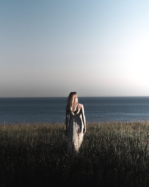 바다 근처 잔디밭을 걷고 인쇄 된 긴 드레스를 입고 여자