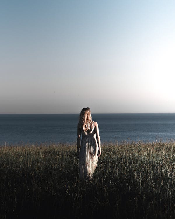 Free Woman Wearing A Printed Long Dress Walking on Grass Field Near The Sea Stock Photo