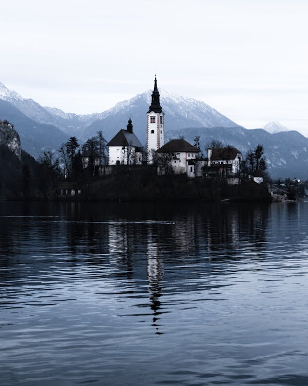 Free Low Angle Shot Of A Church On A River Islet Surrounded By Snow-Capped Mountains Stock Photo