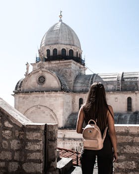 阳光明媚的日子里，一名妇女在一座历史悠久的石头大教堂前观光