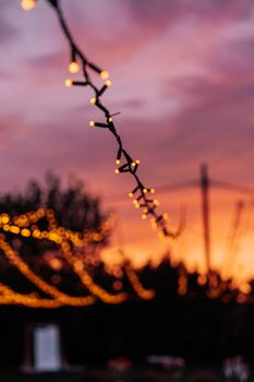 A serene evening scene in Alaaddinbey, Bursa featuring glowing string lights against a vibrant sunset sky.
