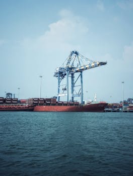 Container ship docked at a bustling industrial port with cranes.
