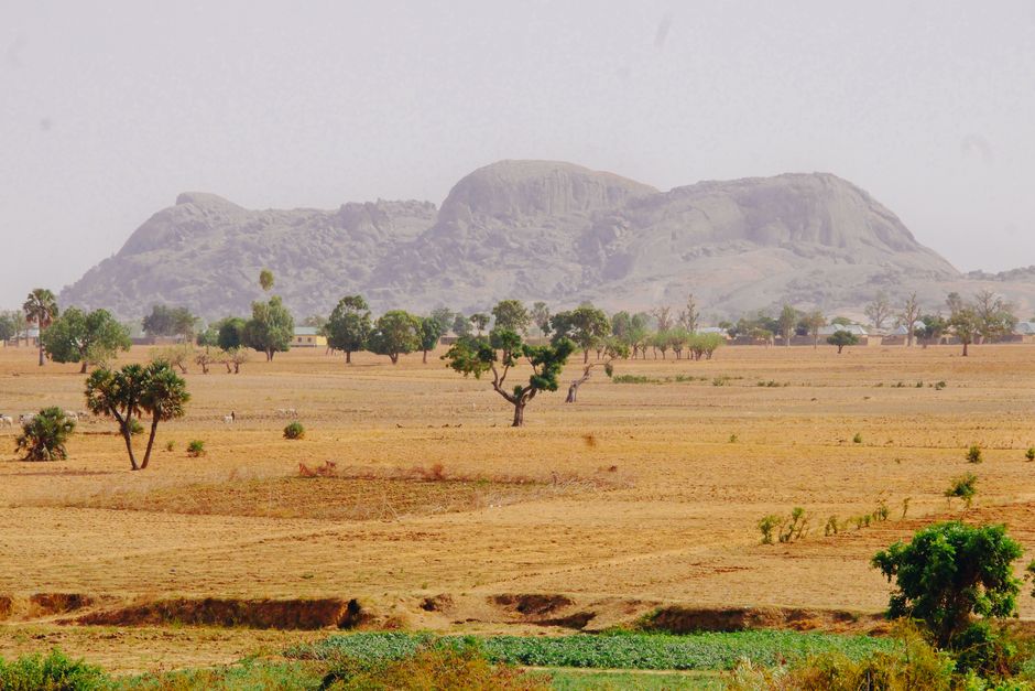 Expansive view of Nigerian savannah with distant hills and trees under a clear sky.