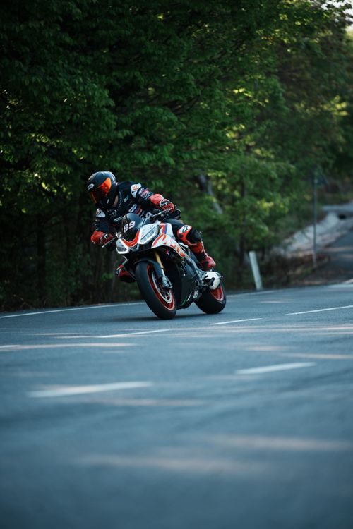 Free A dynamic shot of a biker in full gear racing on a winding road surrounded by lush greenery. Stock Photo