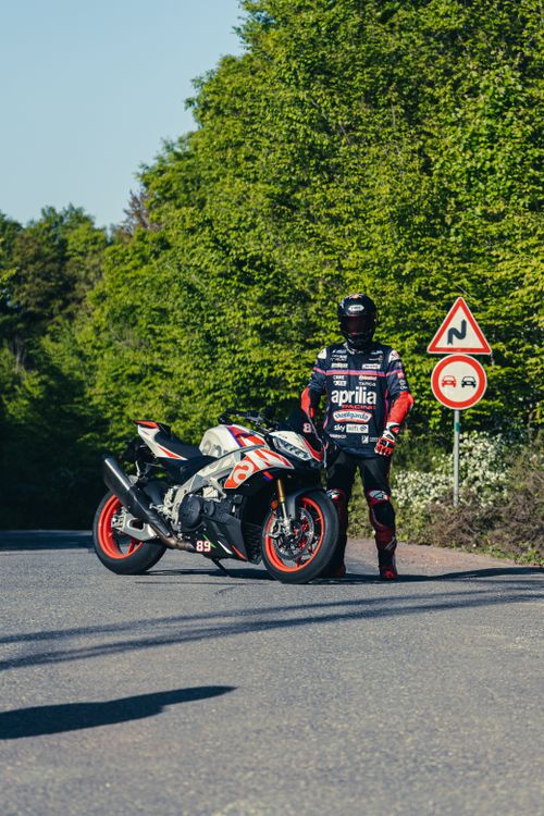 Free Biker stands by sport motorcycle on a scenic forest road during daytime. Stock Photo