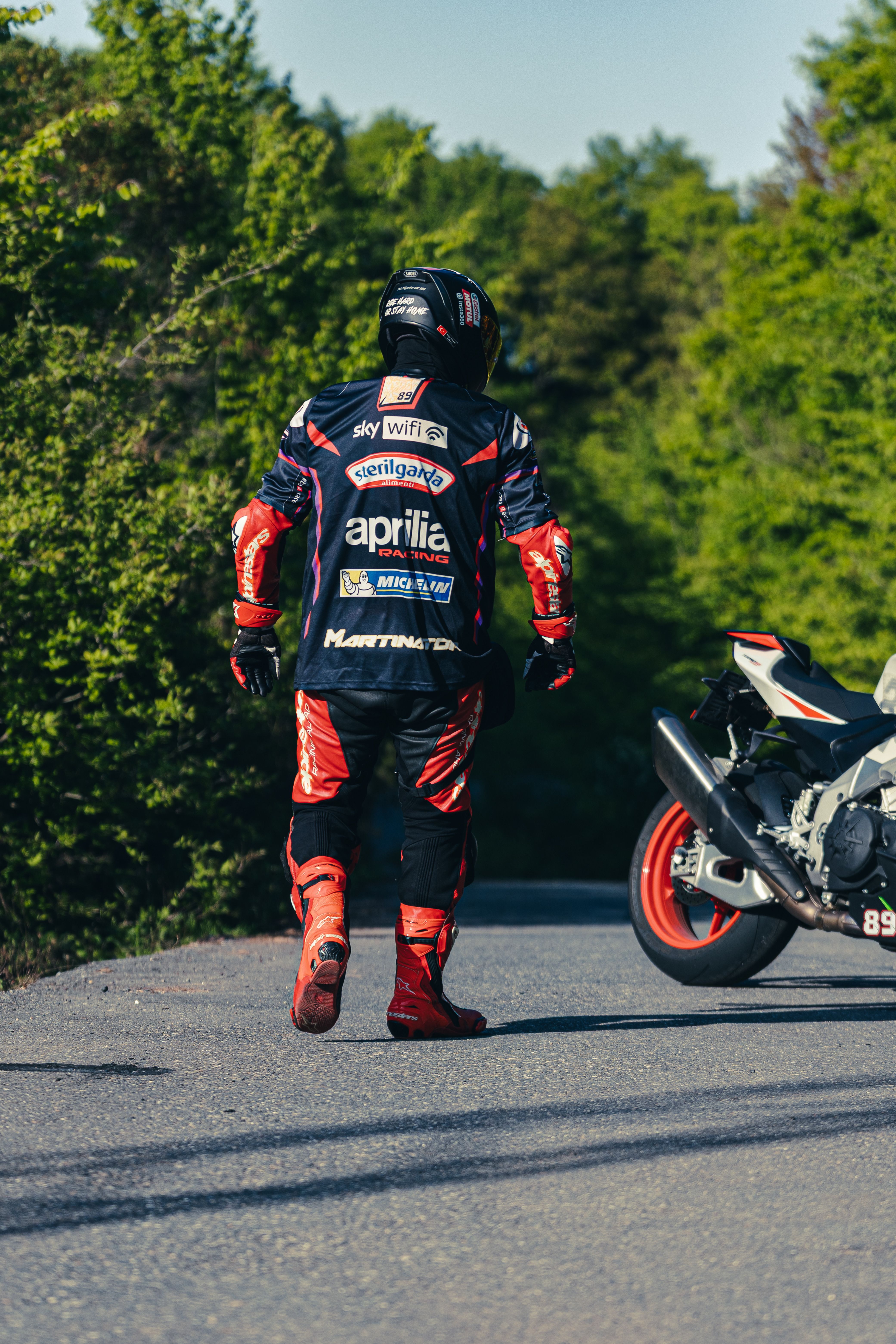 Motorcyclist in protective gear walking on road beside a parked sport bike.