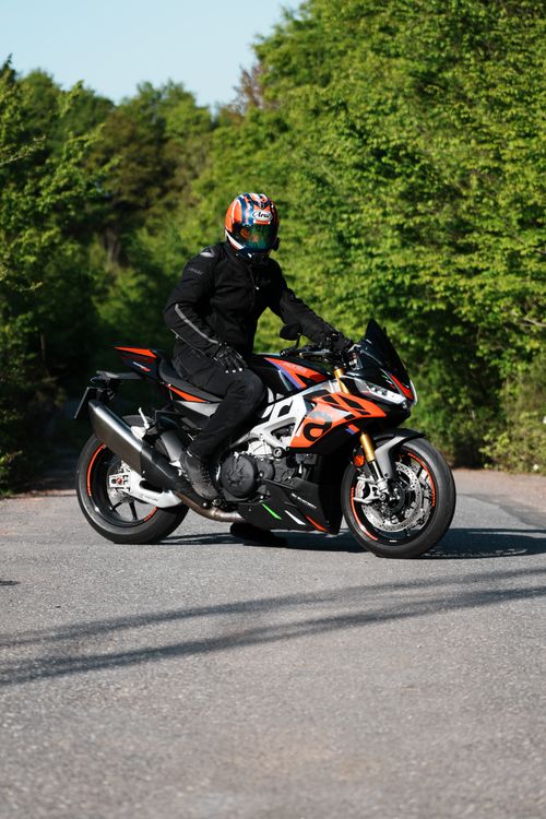 Free Motorcyclist in full gear riding a sport bike on a sunny road through lush greenery. Stock Photo